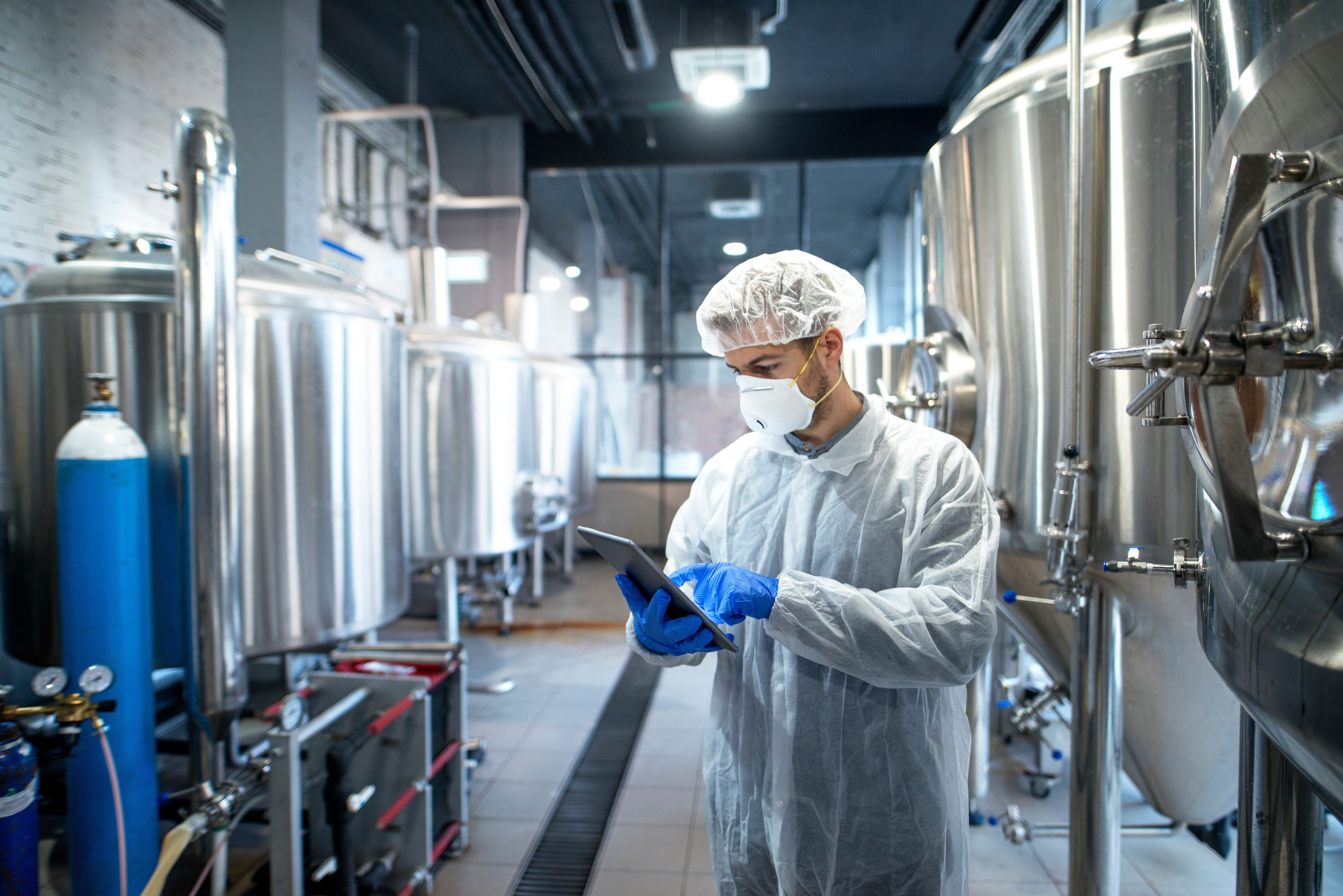 Technologist in white protective uniform controlling industrial process using tablet computer.